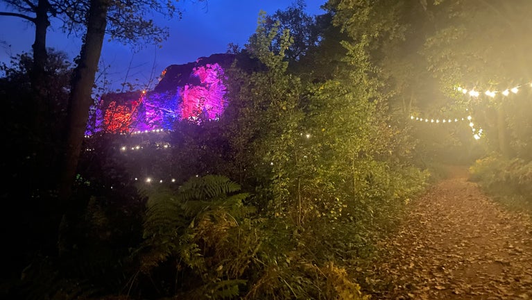 Rock Houses illuminated by pink and blue lights, festoon lights are strung up over a path into the woods.